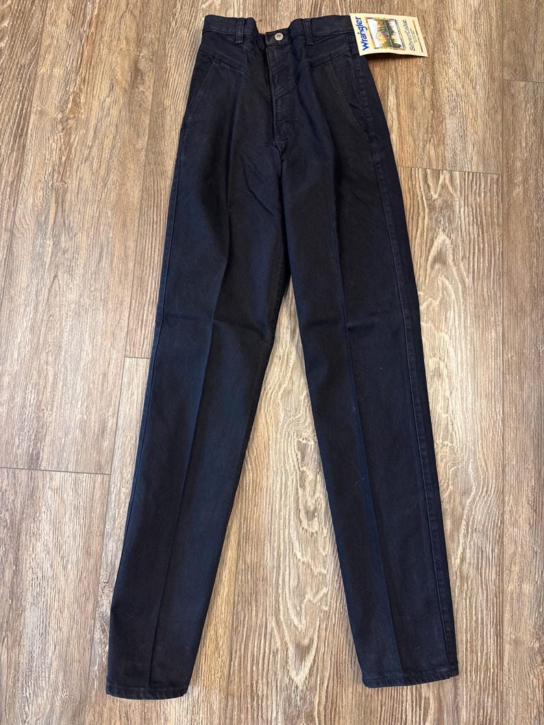 K&ouml;nnte beinhalten: Schwarze Jeans mit hoher Taille und einem Wrangler-Markenetikett. Die Jeans haben eine gerade Beinweite und eine klassische Passform.