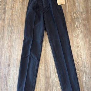 May include: Dark wash denim Wrangler jeans with a high waist and pleated front. The jeans have a button closure and a straight leg. A Wrangler tag is attached to the jeans.