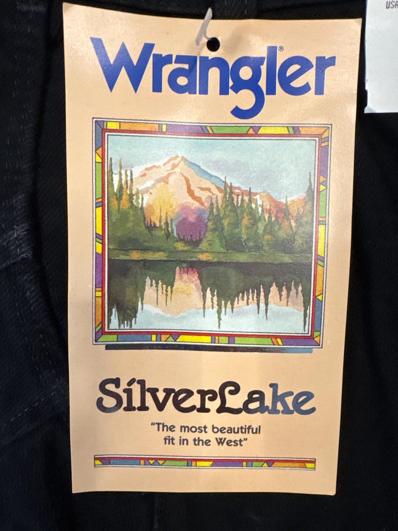 May include: A Wrangler tag with the brand name in blue. The tag features a landscape painting of a lake and mountains, with the text "SilverLake" and the tagline "The most beautiful fit in the West."