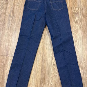 May include: Dark blue denim jeans with a classic five-pocket design. The jeans have a straight leg cut and feature a Wrangler brand tag. The back view shows the pockets and stitching details.