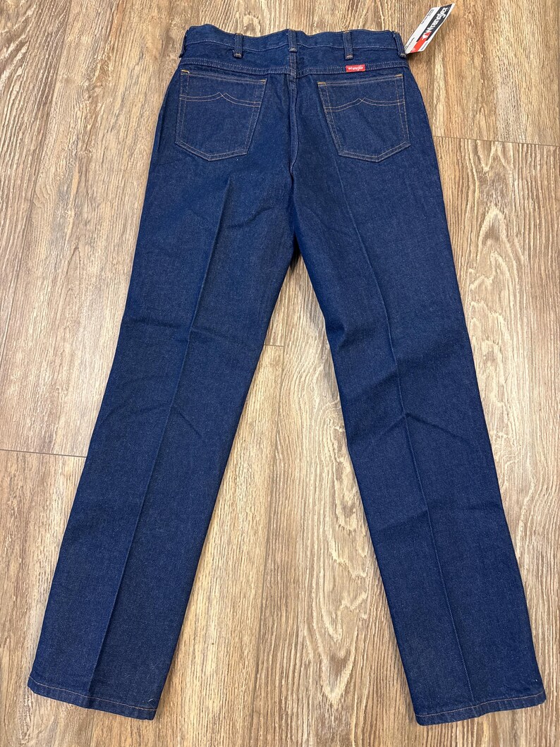 May include: Dark blue denim jeans with a classic five-pocket design. The jeans have a straight leg cut and feature a Wrangler brand tag. The back view shows the pockets and stitching details.