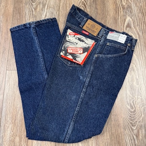 May include: Dark blue Wrangler jeans with a classic five-pocket design. The jeans have a straight leg cut and feature the Wrangler brand label on the back pocket and waistband. A red and white tag reads "American Hero".