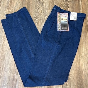 Puede incluir: Vaqueros de mezclilla azul oscuro con un dise&ntilde;o de pierna recta. Los vaqueros tienen una cintura alta y una etiqueta que dice "Silverlake Wrangler". Los vaqueros est&aacute;n doblados sobre una superficie de madera.
