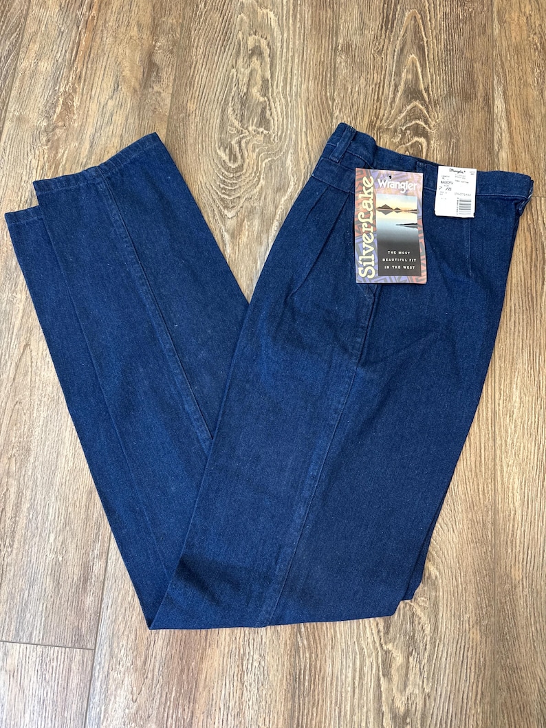 Puede incluir: Vaqueros de mezclilla azul oscuro con un dise&ntilde;o de pierna recta. Los vaqueros tienen una cintura alta y una etiqueta que dice "Silverlake Wrangler". Los vaqueros est&aacute;n doblados sobre una superficie de madera.