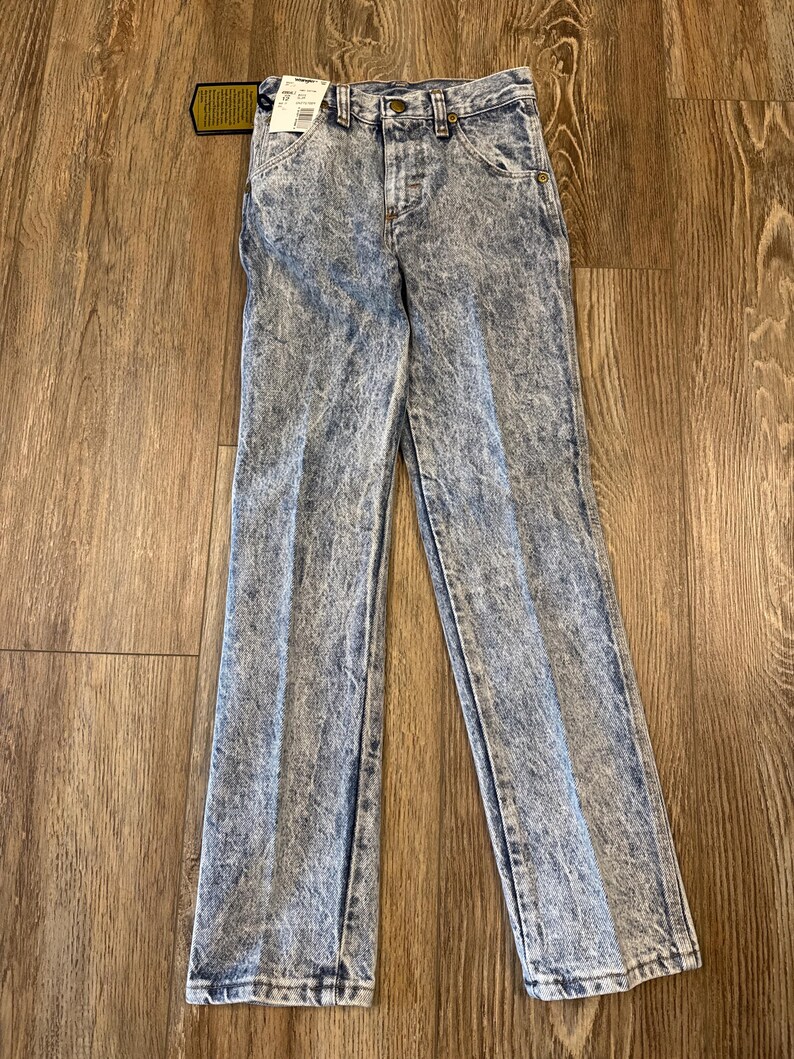 K&ouml;nnte beinhalten: Jeans aus Acid-Wash-Denim mit klassischem F&uuml;nf-Taschen-Design. Die Jeans haben ein hellblaues und wei&szlig;es Marmormuster, einen Knopf- und Rei&szlig;verschluss und ein Etikett am Bund. Die Jeans sind gerade geschnitten.