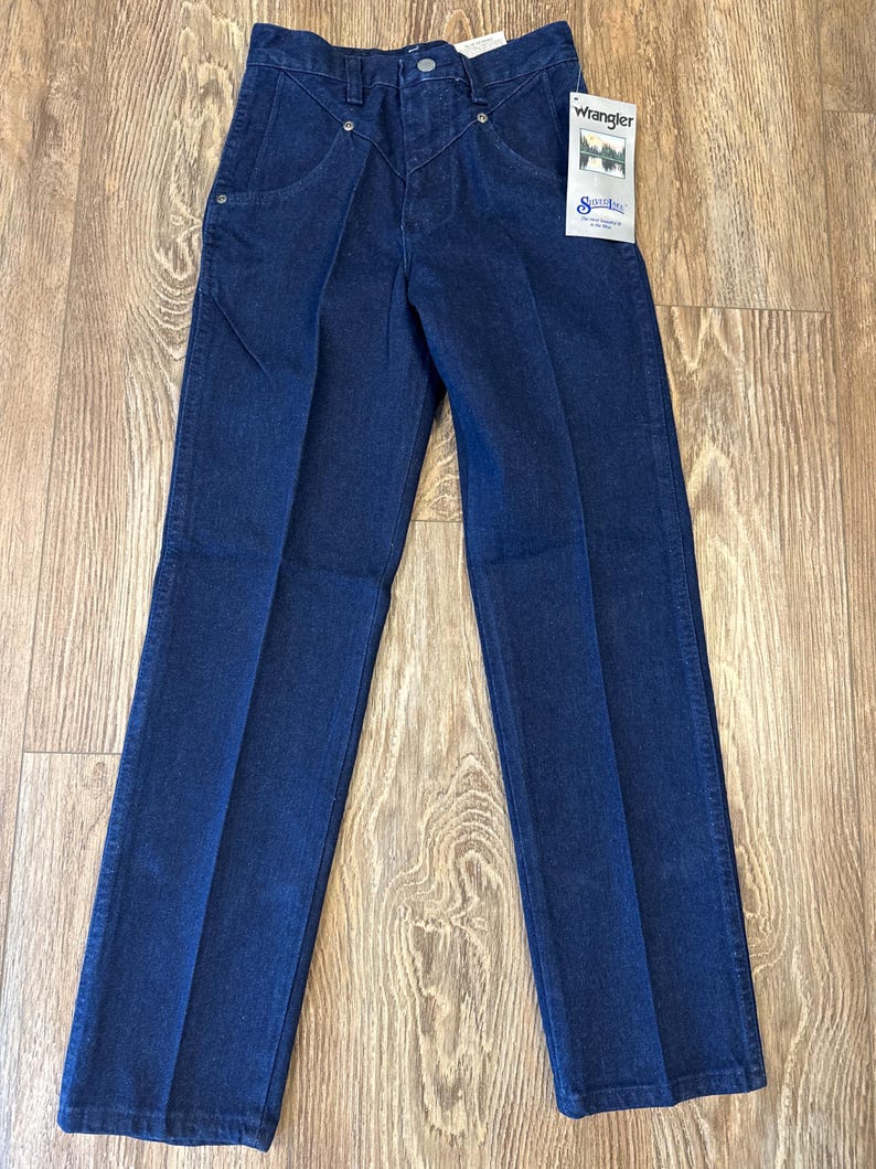May include: Dark blue denim jeans with a classic fit. Features include a button and zipper closure, front pockets, and a Wrangler brand tag. The jeans have a straight leg design.