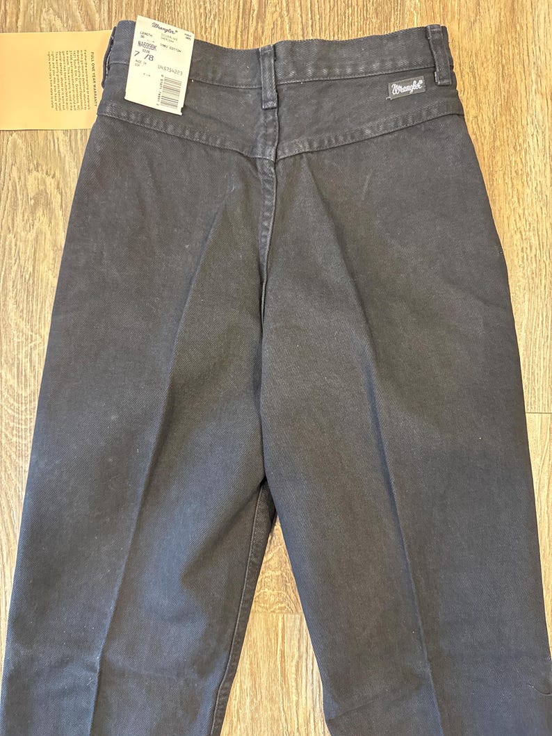 K&ouml;nnte beinhalten: Schwarze Wrangler Jeans mit hoher Taille und geradem Bein. Die Jeans haben ein Etikett am hinteren Bund, auf dem "Wrangler" und "2.78" steht.