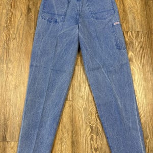 May include: Light blue denim jeans with two back pockets and a small side pocket. The jeans have a classic five-pocket design and a straight leg fit. The Wrangler tag is visible.