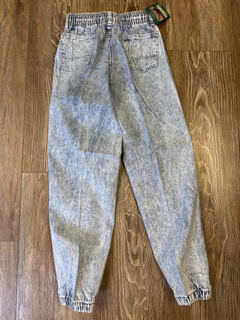 K&ouml;nnte beinhalten: Jeans aus Acid-Wash-Denim mit elastischem Bund und zwei Ges&auml;&szlig;taschen. Die Jeans hat ein konisches Bein mit elastischen B&uuml;ndchen an den Kn&ouml;cheln. Ein Wrangler-Etikett ist angebracht.