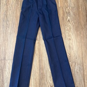 May include: Dark blue denim pants with a classic five-pocket design. The pants have a button and zipper closure, with a straight leg cut. The stitching is a contrasting light brown color. The pants are laid flat on a wooden surface.