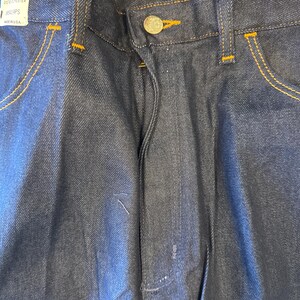 Peut inclure: Un jean en denim bleu fonc&eacute; avec un bouton marron et des coutures orange. Le jean porte une &eacute;tiquette de taille indiquant "34 32" et "8411PS".