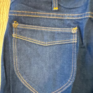May include: A pair of dark blue denim jeans with a back pocket featuring a contrasting dark blue fabric and orange stitching.
