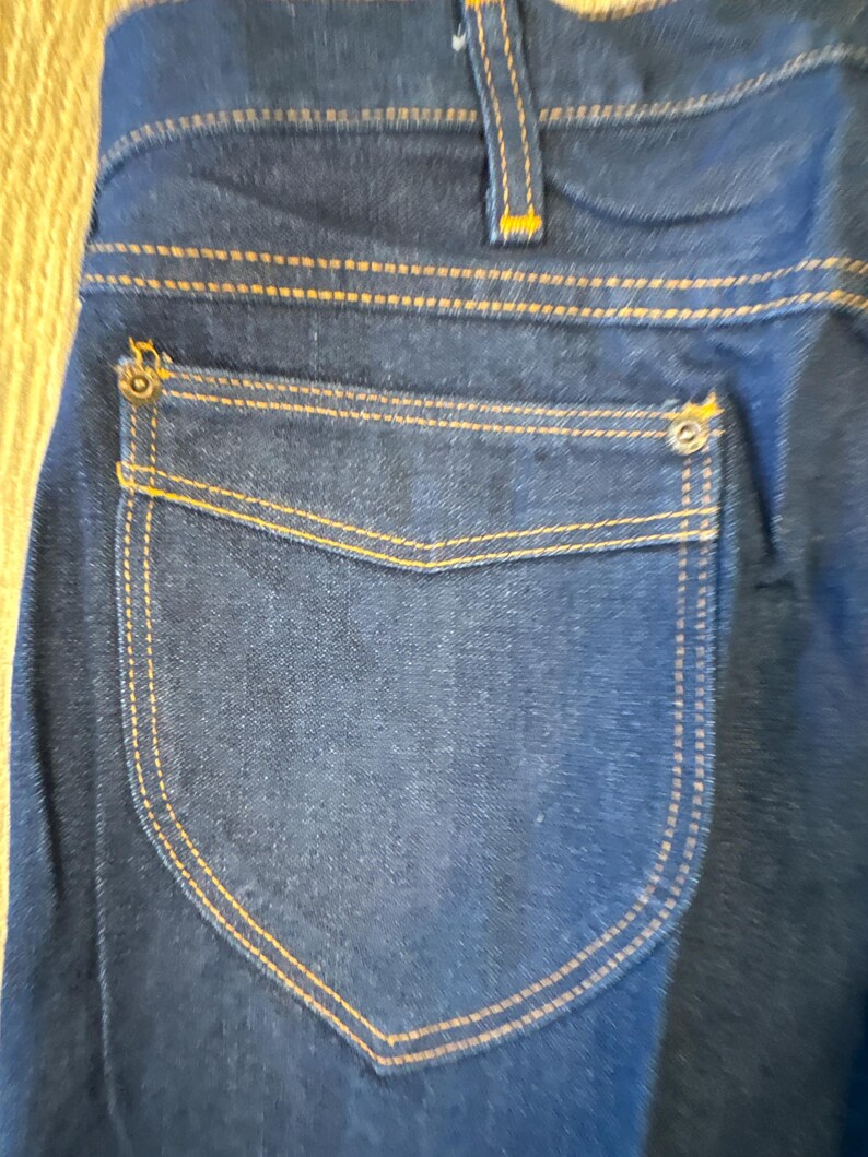 May include: A pair of dark blue denim jeans with a back pocket featuring a contrasting dark blue fabric and orange stitching.