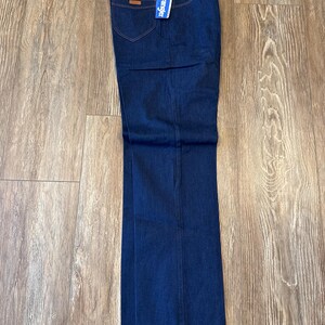 May include: A pair of dark blue denim jeans with a Wrangler brand tag attached. The jeans have a straight leg style and are folded at the bottom.