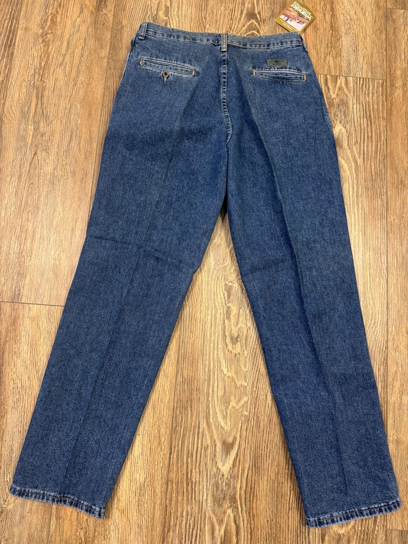 May include: Blue denim jeans, seen from the rear, featuring a button closure and pockets. The jeans have a classic, straight-leg cut and a small tag attached to the back pocket. The denim has a medium wash.