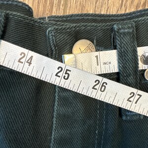 May include: Close-up of a dark green fabric with a white measuring tape that reads "24", "25", "26", "27", and "1 inch".