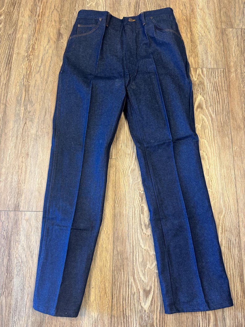 May include: Dark blue denim pants with a classic straight leg design. The pants feature a button and zipper closure, front pockets, and belt loops. The denim has a slight sheen, and the pants are neatly pressed.