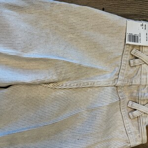 May include: White corduroy trousers with a striped pattern and a Wrangler label. The trousers have a tie at the waist and a small Wrangler logo patch on the back.