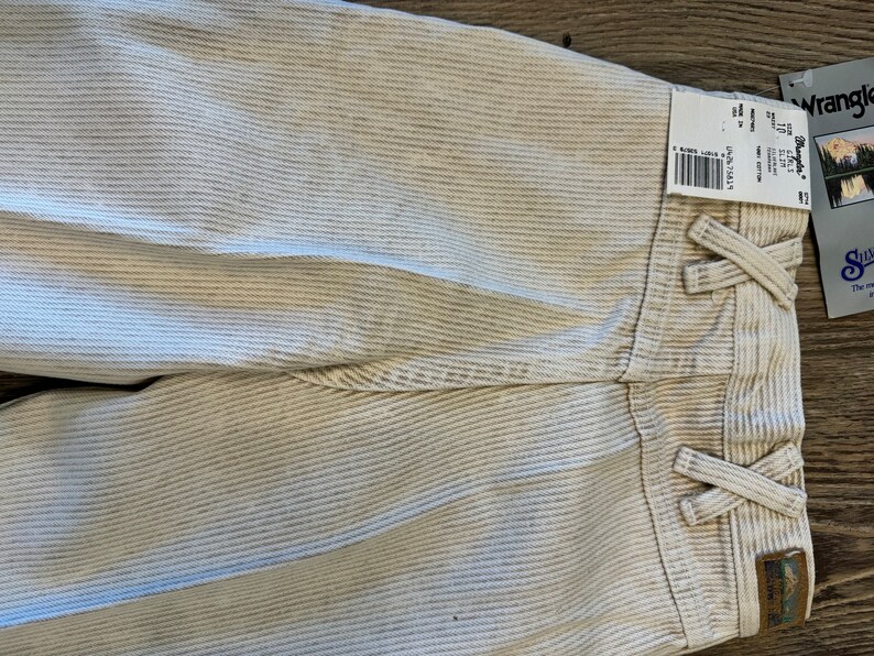 May include: White corduroy trousers with a striped pattern and a Wrangler label. The trousers have a tie at the waist and a small Wrangler logo patch on the back.