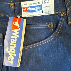 May include: A pair of blue denim jeans with a Wrangler brand tag. The tag says "Full 1 Year Warranty" and "100% Cotton". The size is 36 L (91 cm) and the style number is 86446PW. The jeans are made in the USA.