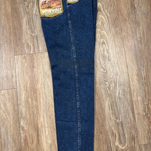 Puede incluir: Vaqueros Wrangler azul oscuro de corte relajado con etiquetas adjuntas. Los vaqueros tienen un dise&ntilde;o cl&aacute;sico de cinco bolsillos y una pernera recta. Las etiquetas presentan el logotipo de Wrangler y un gr&aacute;fico de un vaquero. Los vaqueros est&aacute;n hechos de denim duradero.