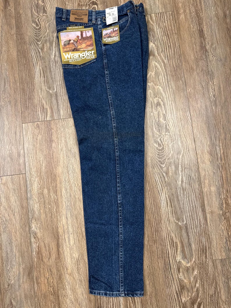 Puede incluir: Vaqueros Wrangler azul oscuro de corte relajado con etiquetas adjuntas. Los vaqueros tienen un dise&ntilde;o cl&aacute;sico de cinco bolsillos y una pernera recta. Las etiquetas presentan el logotipo de Wrangler y un gr&aacute;fico de un vaquero. Los vaqueros est&aacute;n hechos de denim duradero.