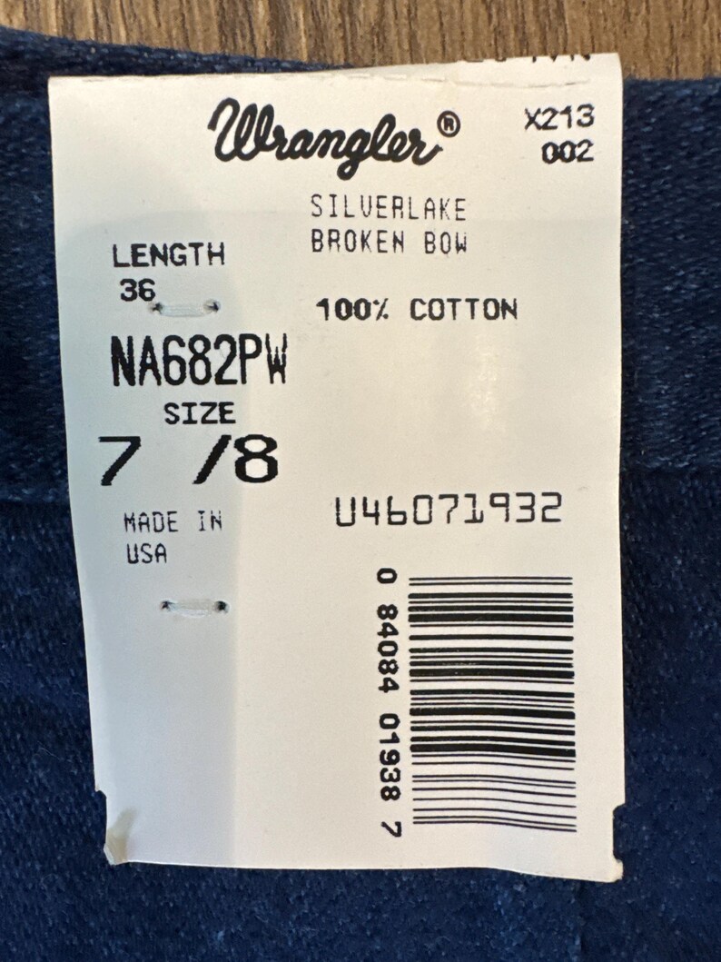 Puede incluir: Una etiqueta blanca con el logo de Wrangler y texto que incluye "SILVERLAKE BROKEN BOW", "100% COTTON" y "SIZE 7/8". La etiqueta tambi&eacute;n indica una longitud de 91 cm y est&aacute; hecha en EE. UU.