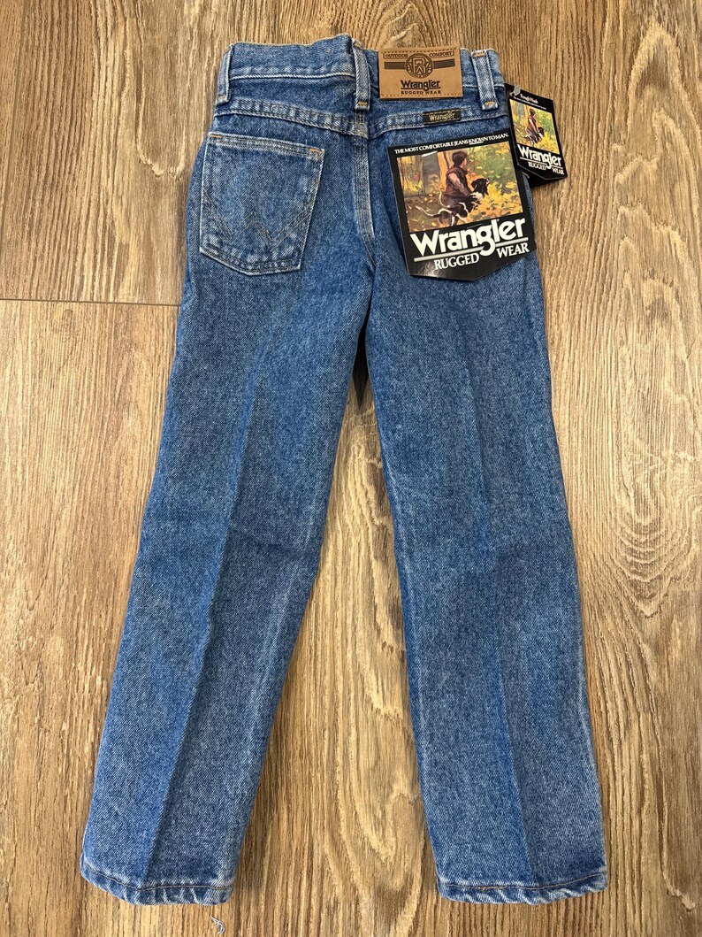 Puede incluir: Un par de pantalones vaqueros azules con una etiqueta de Wrangler en el bolsillo trasero. Los pantalones tienen una pierna recta y un ajuste cl&aacute;sico.