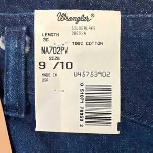 Puede incluir: Primer plano de tela vaquera azul oscuro con una etiqueta blanca adjunta. La etiqueta dice "Wrangler" e incluye detalles como "SILVERLAKE ODESSA", "100% COTTON", talla 9/10 y una longitud de 91 cm. La etiqueta tambi&eacute;n tiene un c&oacute;digo de barras.