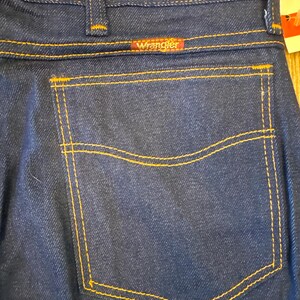 Peut inclure: Un jean en denim bleu fonc&eacute; avec une poche arri&egrave;re et une &eacute;tiquette Wrangler. Le jean est fabriqu&eacute; aux &Eacute;tats-Unis.