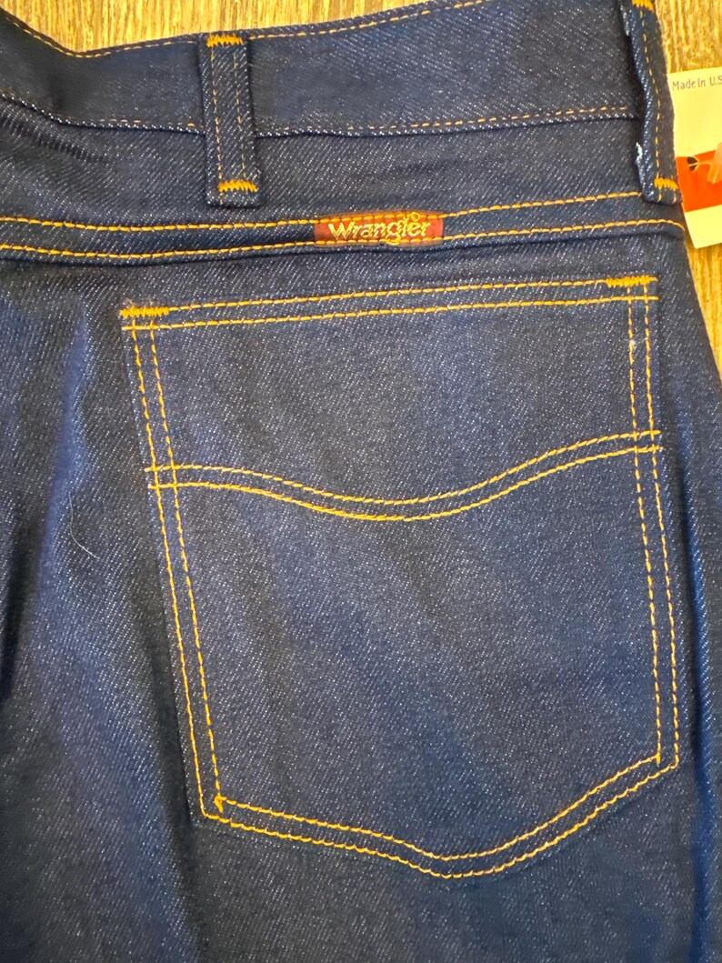 Peut inclure: Un jean en denim bleu fonc&eacute; avec une poche arri&egrave;re et une &eacute;tiquette Wrangler. Le jean est fabriqu&eacute; aux &Eacute;tats-Unis.