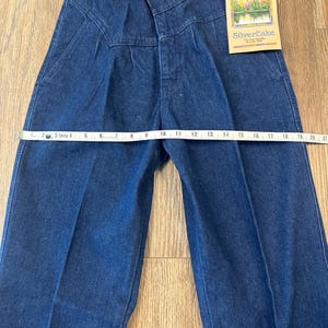 Puede incluir: Vaqueros Wrangler Silverlake de mezclilla azul oscuro con cintura alta y cierre de bot&oacute;n. Los vaqueros tienen una pernera recta y una etiqueta que dice "Wrangler Silverlake". La cintura mide aproximadamente 25 cm.