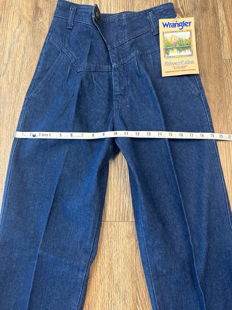 Puede incluir: Vaqueros Wrangler Silverlake de mezclilla azul oscuro con cintura alta y cierre de bot&oacute;n. Los vaqueros tienen una pernera recta y una etiqueta que dice "Wrangler Silverlake". La cintura mide aproximadamente 25 cm.