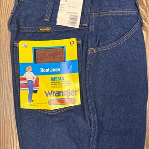 K&ouml;nnte beinhalten: Dunkelblaue Wrangler Bootcut-Jeans mit gelb-braunem Etikett. Das Etikett lautet "Boot Jean" und "Misses Wrangler No-Fault Heavy Weight Denim". Die Jeans haben ein klassisches F&uuml;nf-Taschen-Design und ein Wrangler-Label.