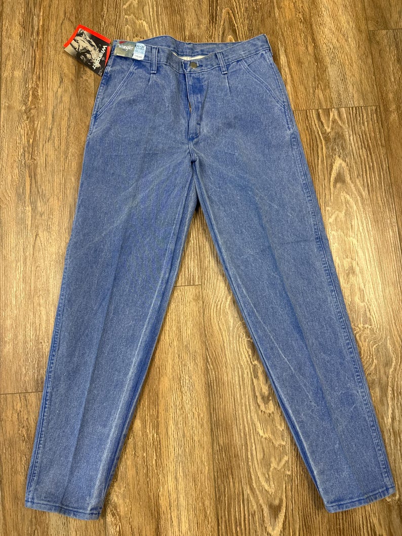 May include: Light blue denim jeans with a faded wash. The jeans have a classic five-pocket design, a button and zipper closure, and a straight leg. A red and white tag is attached to the jeans.