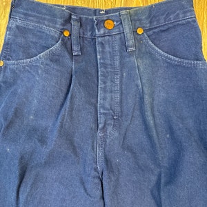 May include: A pair of dark blue denim jeans with a button fly and five pockets. The jeans have a faded look and are made of a thick, durable fabric.