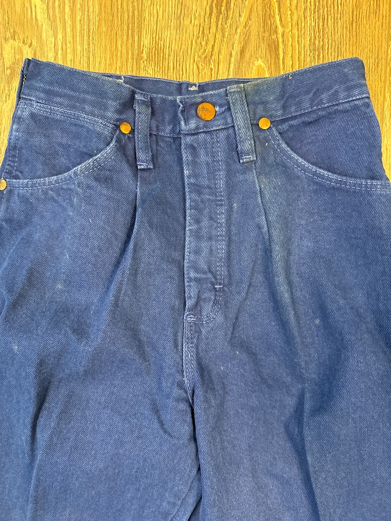 May include: A pair of dark blue denim jeans with a button fly and five pockets. The jeans have a faded look and are made of a thick, durable fabric.