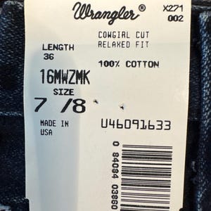 May include: A white tag with the Wrangler logo and text. The tag reads "COWGIRL CUT RELAXED FIT" and "100% COTTON". It also indicates a length of 36 inches and a size of 7/8. The tag is marked "MADE IN USA".