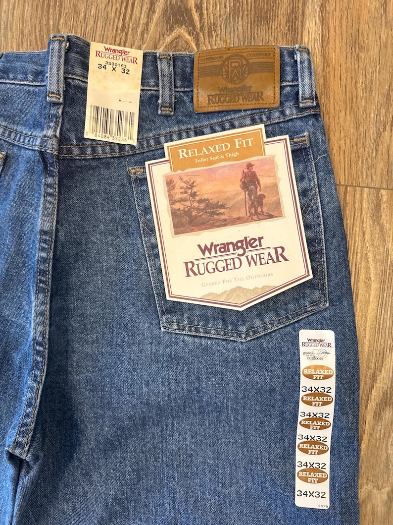 May include: A pair of blue denim jeans with a brown leather patch that says "Wrangler Rugged Wear". The jeans are size 34x32 and have a relaxed fit.