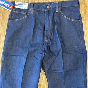 May include: A pair of dark blue denim jeans with a brown leather patch on the back waistband. The jeans have a classic five-pocket style and a straight leg.