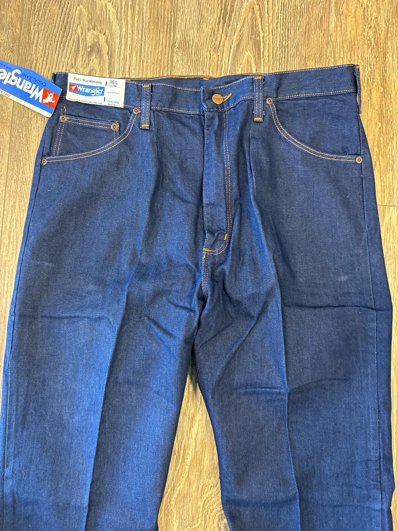 May include: A pair of dark blue denim jeans with a brown leather patch on the back waistband. The jeans have a classic five-pocket style and a straight leg.
