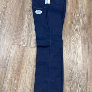 May include: Dark blue Wrangler jeans with orange stitching and a Flex Fit tag. The jeans have a straight leg cut and are folded neatly. A white tag with the Wrangler logo is attached to the back pocket.
