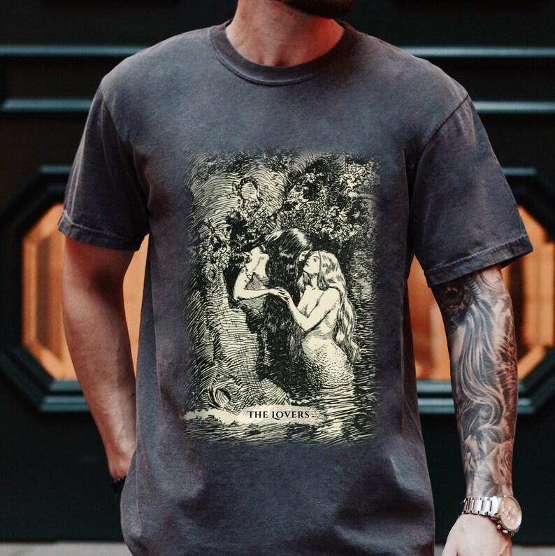Pode incluir: Uma camiseta cinza escura com uma ilustra&ccedil;&atilde;o vintage de duas figuras em um cen&aacute;rio de floresta. A ilustra&ccedil;&atilde;o &eacute; em preto e branco e apresenta o texto "THE LOVERS".