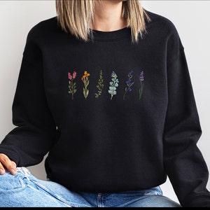 Puede incluir: Sudadera negra con un arcoíris de flores impreso en la parte delantera. Las flores están en una línea a través del centro de la camisa.