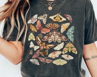 May include: A dark gray t-shirt with a colorful print of various butterflies and moths. The print features a variety of colors, including shades of blue, green, yellow, orange, and red.