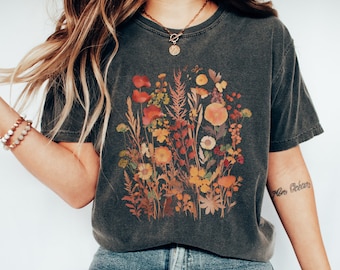 May include: A dark gray t-shirt with a floral print featuring pressed flowers in shades of orange, red, and yellow. The flowers are arranged in a bouquet-like design.