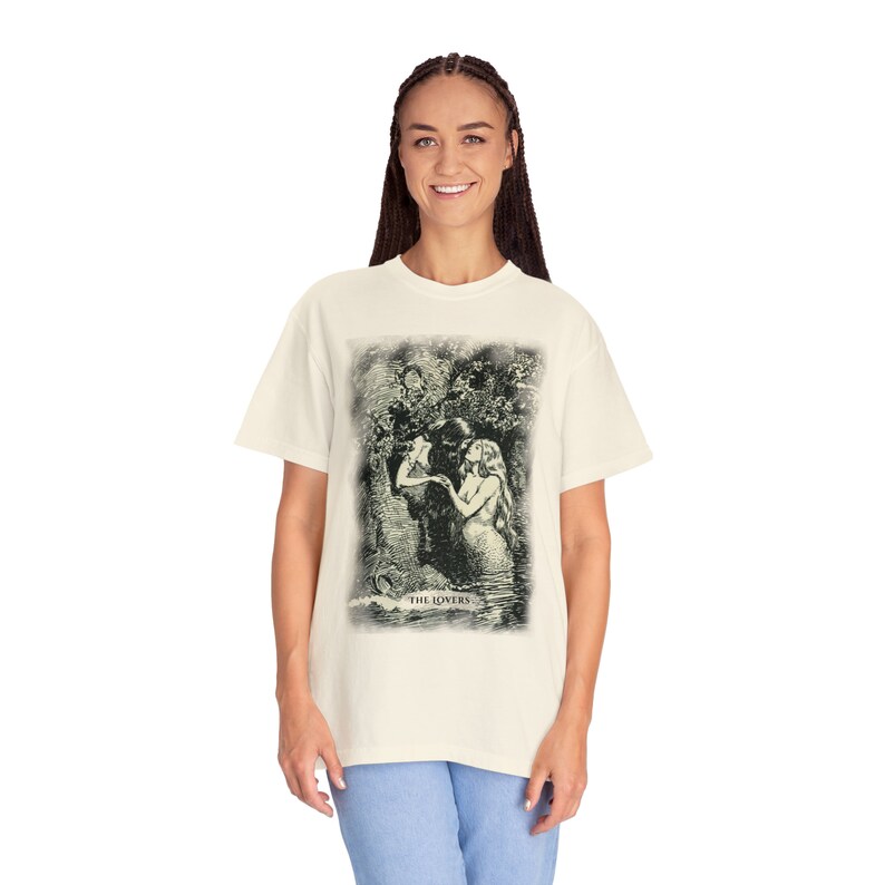 Pode incluir: Uma camiseta branca com uma ilustra&ccedil;&atilde;o vintage de um casal se abra&ccedil;ando em um cen&aacute;rio de floresta. A ilustra&ccedil;&atilde;o &eacute; em tons de verde e preto e inclui o texto "THE LOVERS".