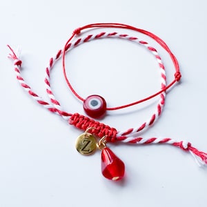 Peut inclure: Bracelet en cordon rouge et blanc avec un charme œil maléfique rouge et un charme en or avec la lettre "Z" qui pend. Le bracelet a également un charme en forme de larme rouge.