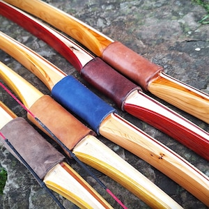 May include: Five wooden bows with leather and fabric grips. The bows are arranged in a row, with the tips pointing to the right. The bows are made of different types of wood, and each has a unique finish.
