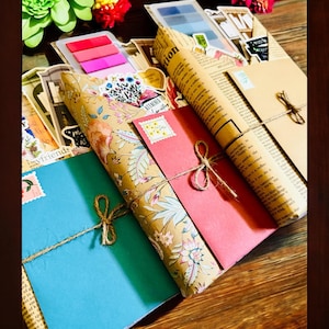May include: A collection of stationery items, including envelopes, paper rolls, and notepads. The items are wrapped in patterned paper and tied with twine. The color palette includes pink, blue, beige, and floral patterns, suggesting a theme of vintage or handmade crafts.